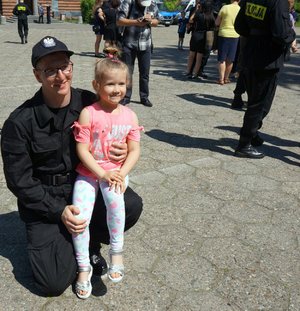Policjant trzymający na kolanie małą dziewczynkę.