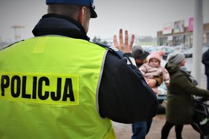 Policjant macha dziecku, które trzyma na rękach jego tata.