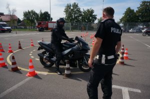 motocyklista na motorze, przed nim tyłem zwrócony policjant, w tle radowóz straży pożarnej oraz karetka pogotowia
