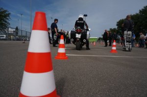 policjant na motorze przodem skierowany do grupy ludzi ustawiony pomiedzy pachołkami