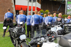 Grupa mężczyzn stoi przy motocyklach w koszulkach z napisem II Pielgrzymka Policyjnych Motocyklistów