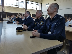 Policjant i strażnicy miejscy siedzą przy stoliku i słuchają przemówienia