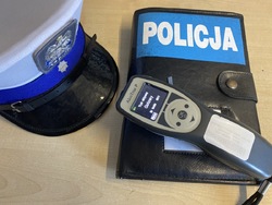 Policyjna czapka leży obok urządzenia do badania stanu trzeźwości i okładce z napisem Policja