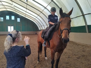 Egzaminatorka wpisuje w kartę ocenę- w tle policyjny jeździec na koniu