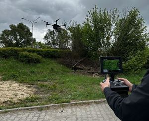 Wyświetlacz drona trzymany w rękach, w tle nad ziemią unosi się dron