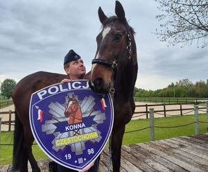 Policjant z koniem pozuje do zdjęcia trzymając w rękach tarcze z napisem Policja Konna Częstochowa