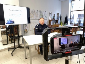 zdjęcie przedstawia policjanta siedzącego za stołem w trakcie debaty