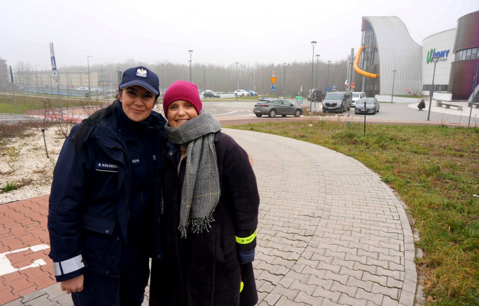 Aktorka Kinga Preis stoi wraz z umundurowaną policjantką,w oddali widać budynek parku wodnego.