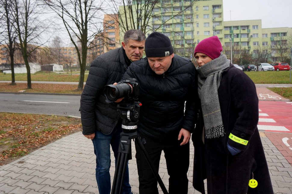 Aktorka Kinga Preis stoi w towarzystwie dwóch nieumundurowanych policjantów w rejonie przejścia dla pieszych. Wszyscy patrzą w obiektyw aparatu. 