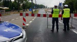 Na zdjęciu policjanci z drogówki zabezpieczają wyścig kolarski, blokują drogę, obok stoi radiowóz.