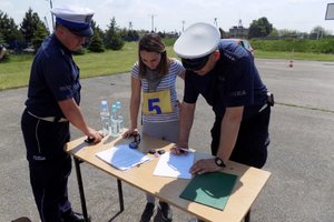 Zdjęcie dwóch policjantów i jednej zawodniczki stojących przy stoliku na placu manewrowym.