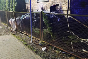 Na zdjęciu widoczny rozbity samochód, który wjechał pomiędzy ogrodzenie a budynek mieszkalny.