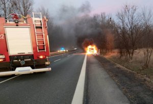 Pojazd straży pożarnej na tle palącego się samochodu.