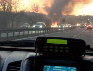 Widok z wnętrza radiowozu na palący się samochód.